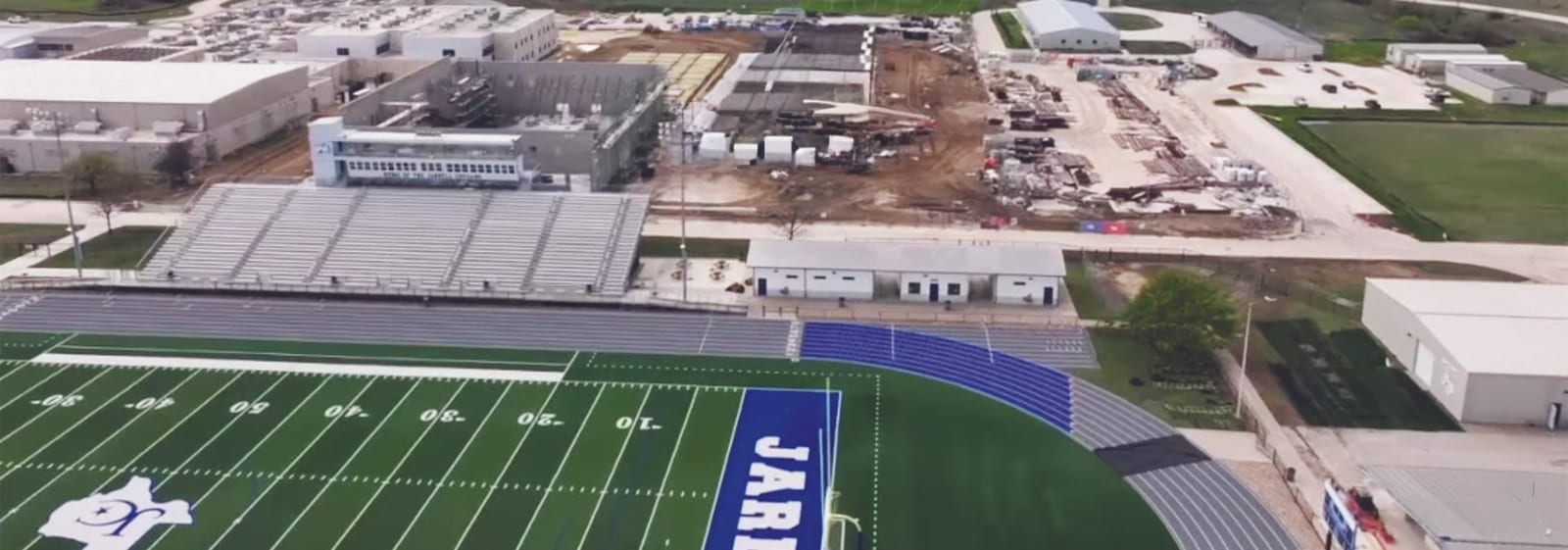 Aerial view of Jarrell ISD campuses with a football field, track, stadium bleachers and buildings under construction