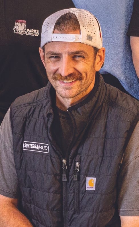 Smiling man with a mustache wearing a backward white cap and a black Sonterra MUD vest.