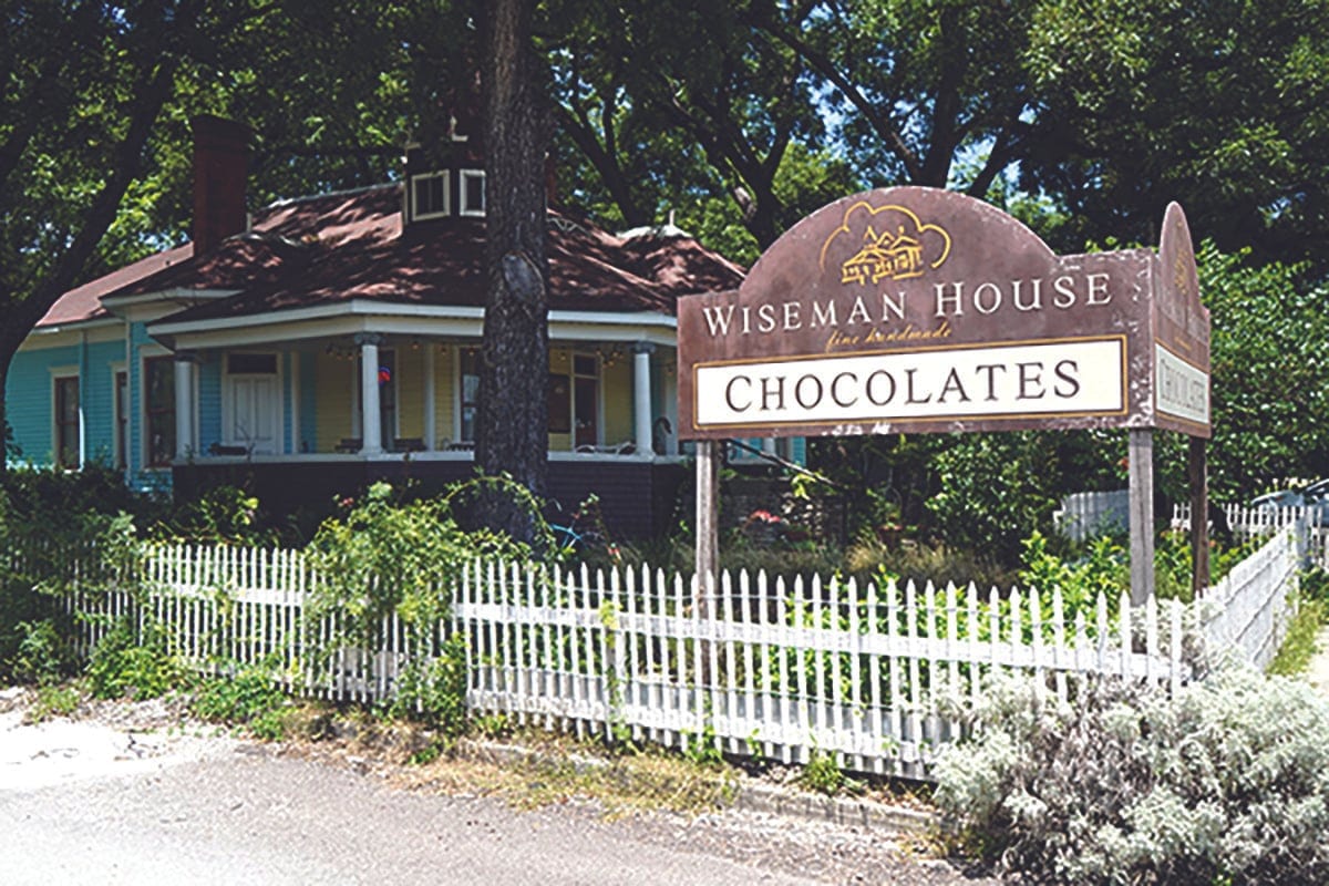 Wiseman House Chocolates sign in front of a restored blue Victorian house with a white picket fence