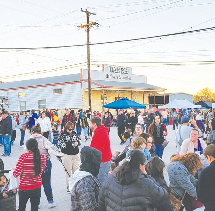 A large crowd gathers in the street outside Danek Hardware & Lumber at an evening community event with tents