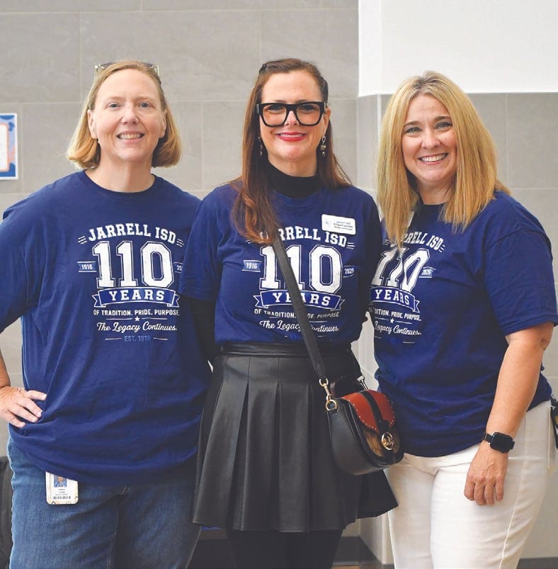Three smiling women wearing matching navy Jarrell ISD 110 Years T-shirts