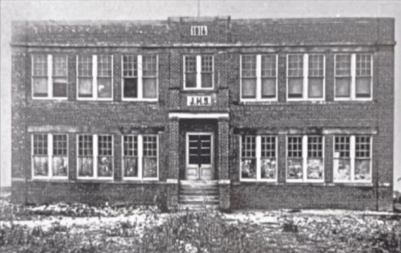 Black-and-white photo of a two-story brick schoolhouse with many windows and 1916 above the entrance